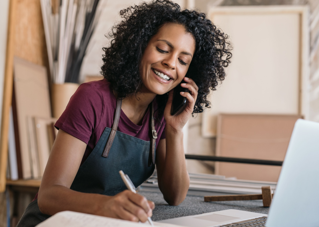 Small business owner speaking on phone taking notes.