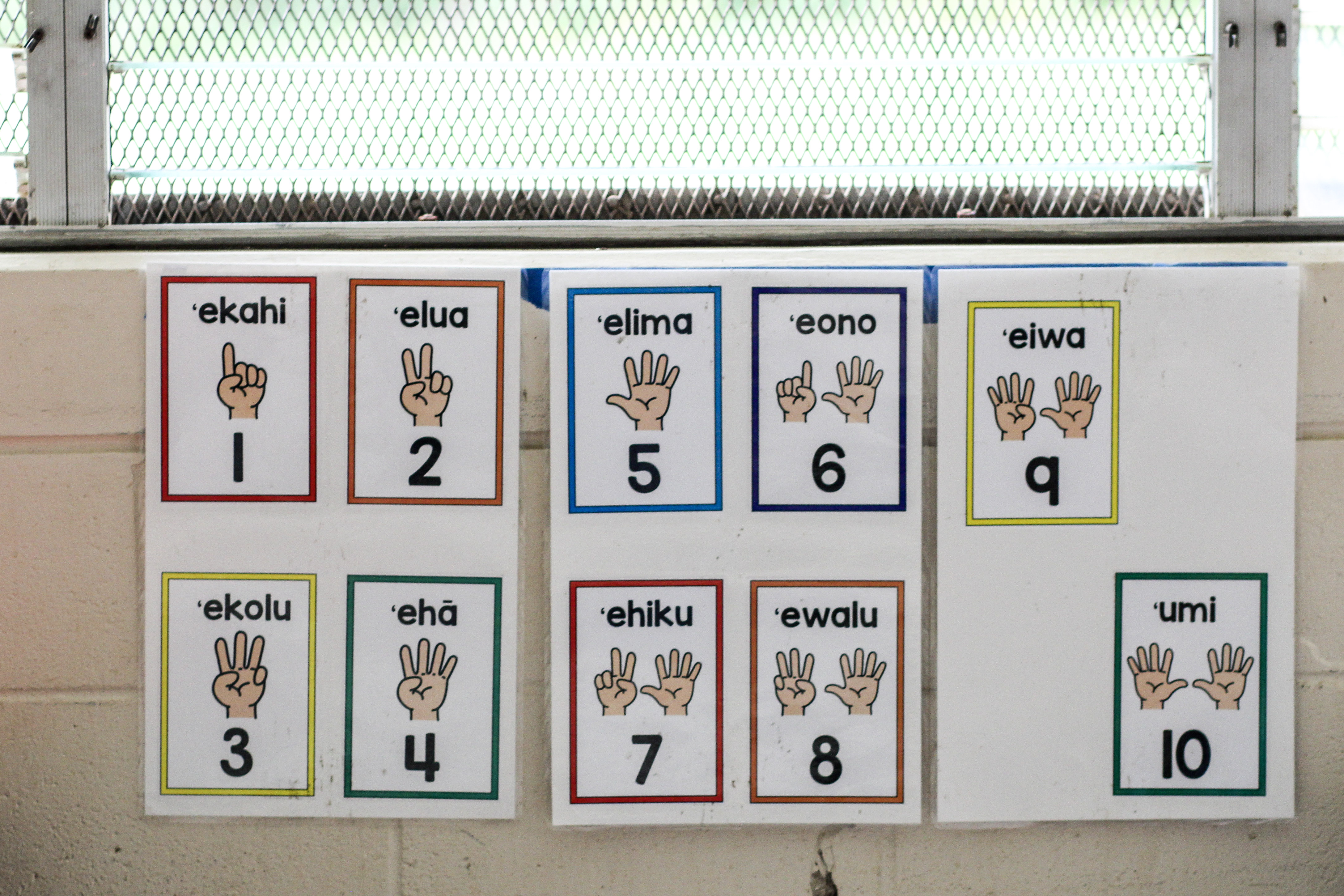 Laminated cards hung on a wall indicate the Hawaiian words for the numbers 1 through 10.