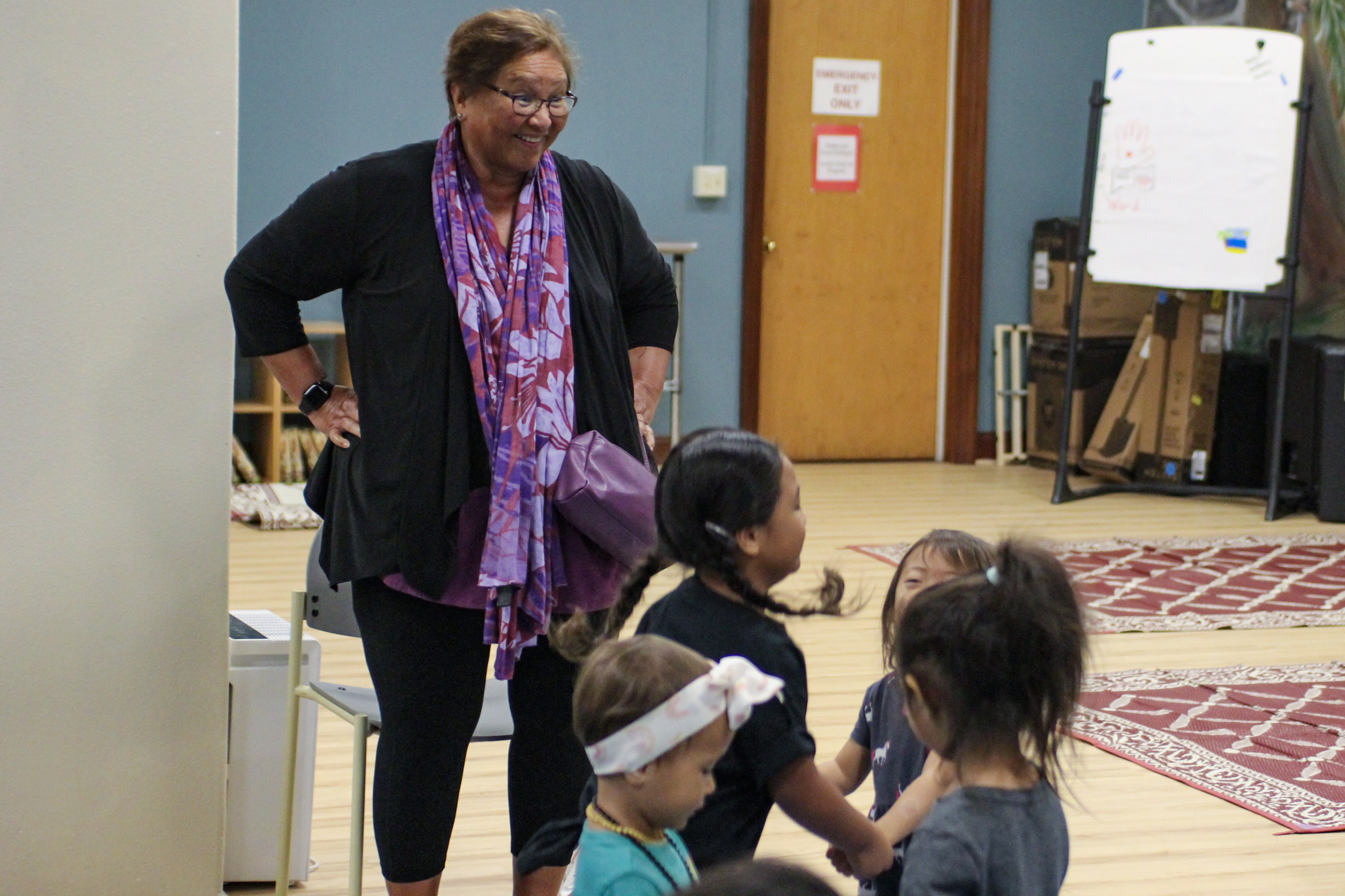  A woman smiles while watching several children interact.