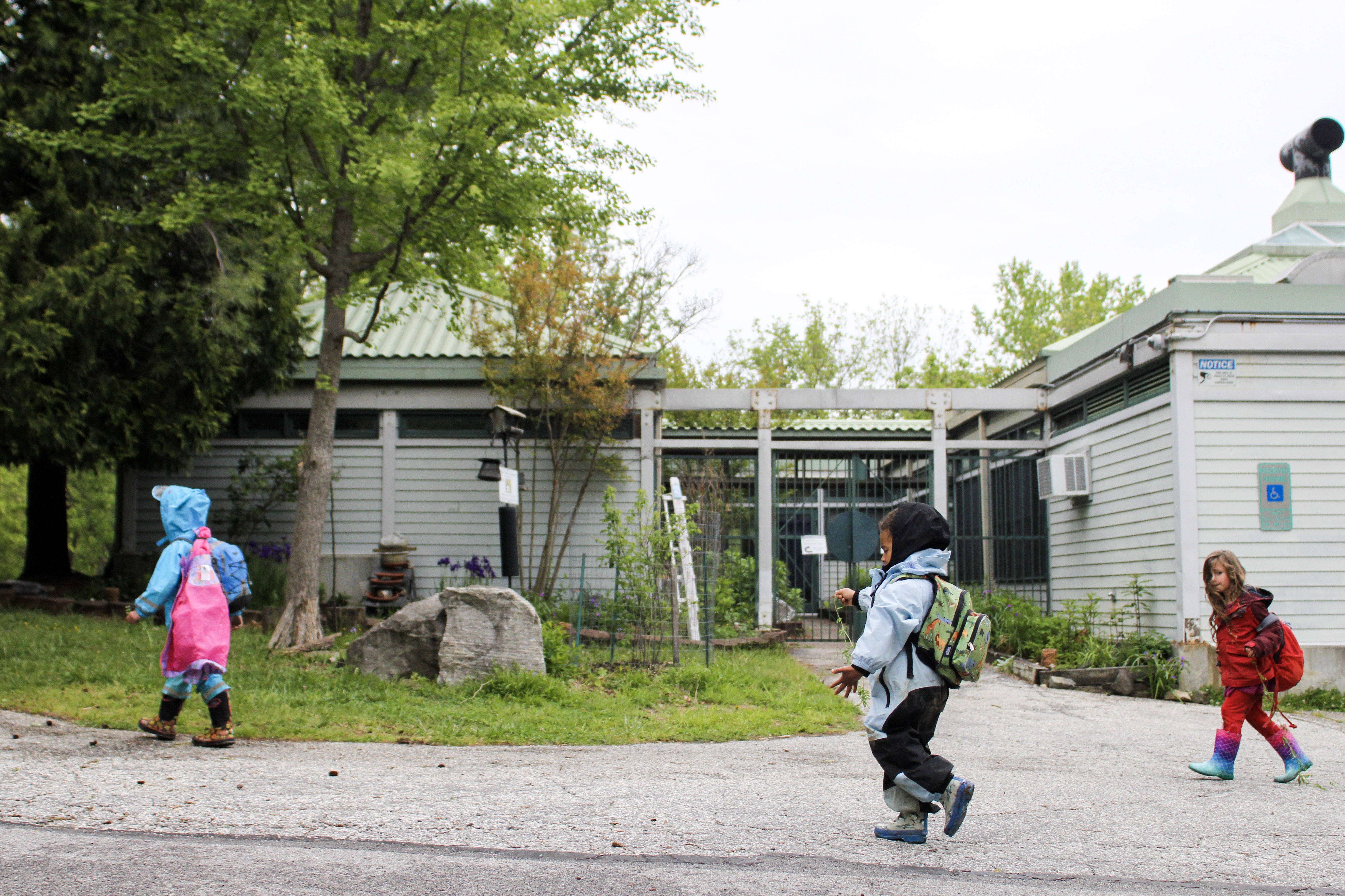  Children in jackets and carrying backpacks walk down a sidewalk. 
