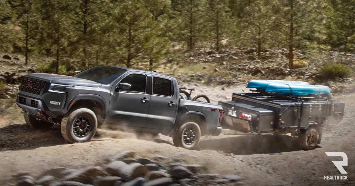 A black Nissan Frontier towing a kayak trailer on a rocky road.