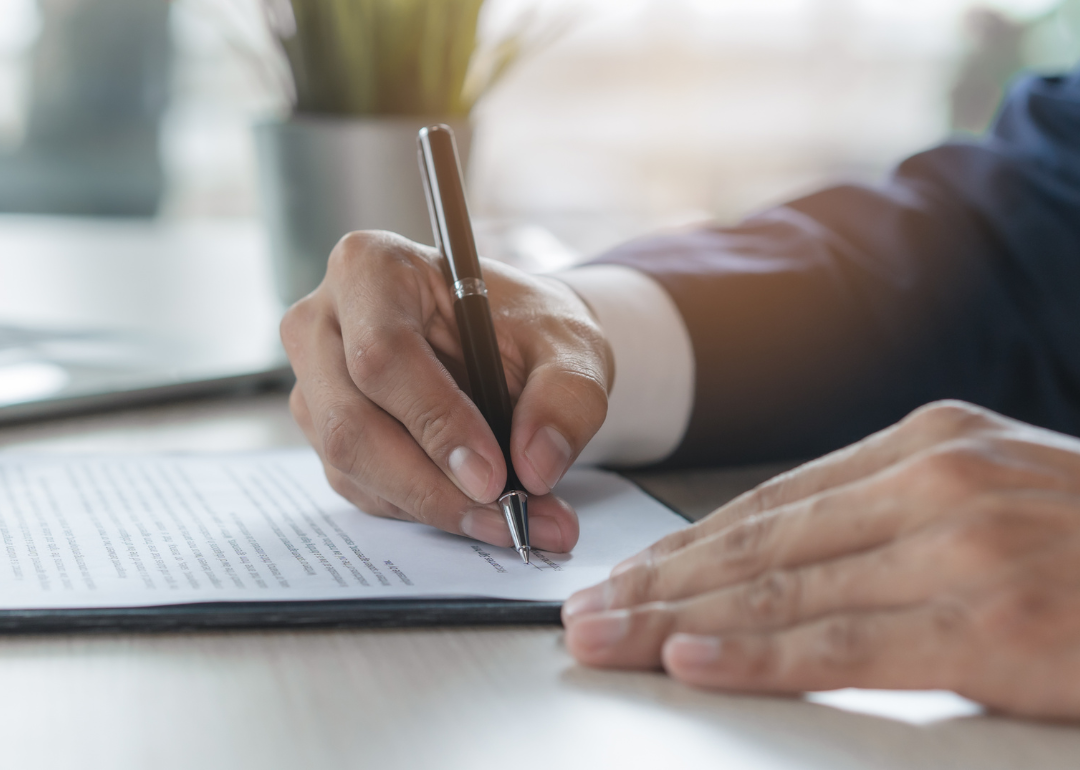 A close-up of a person's hand as they sign a document.