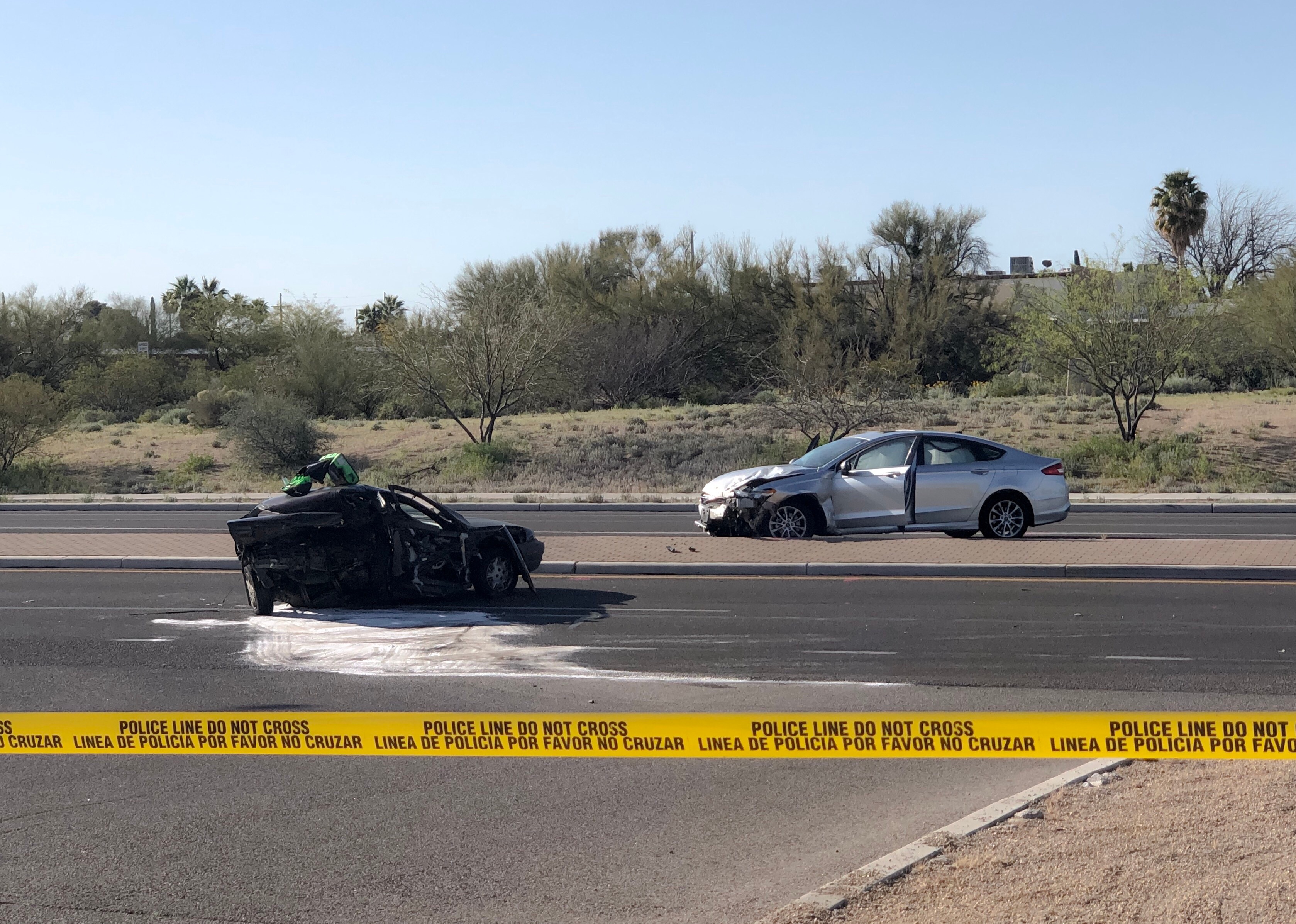 A severe car crash with a yellow police tape saying, do not cross, in English and Spanish.