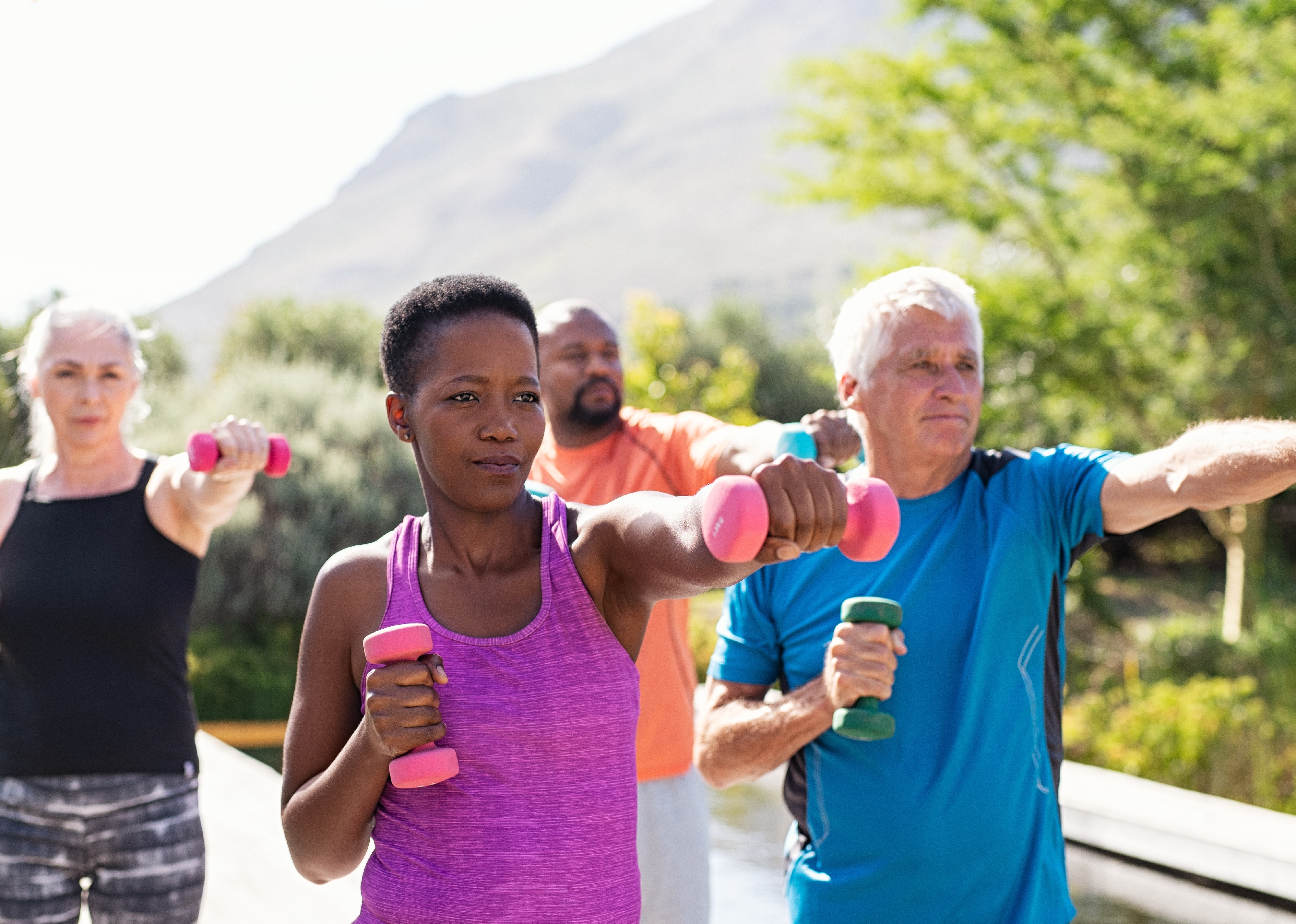 Group of people exercising using dumbbells outdoors.