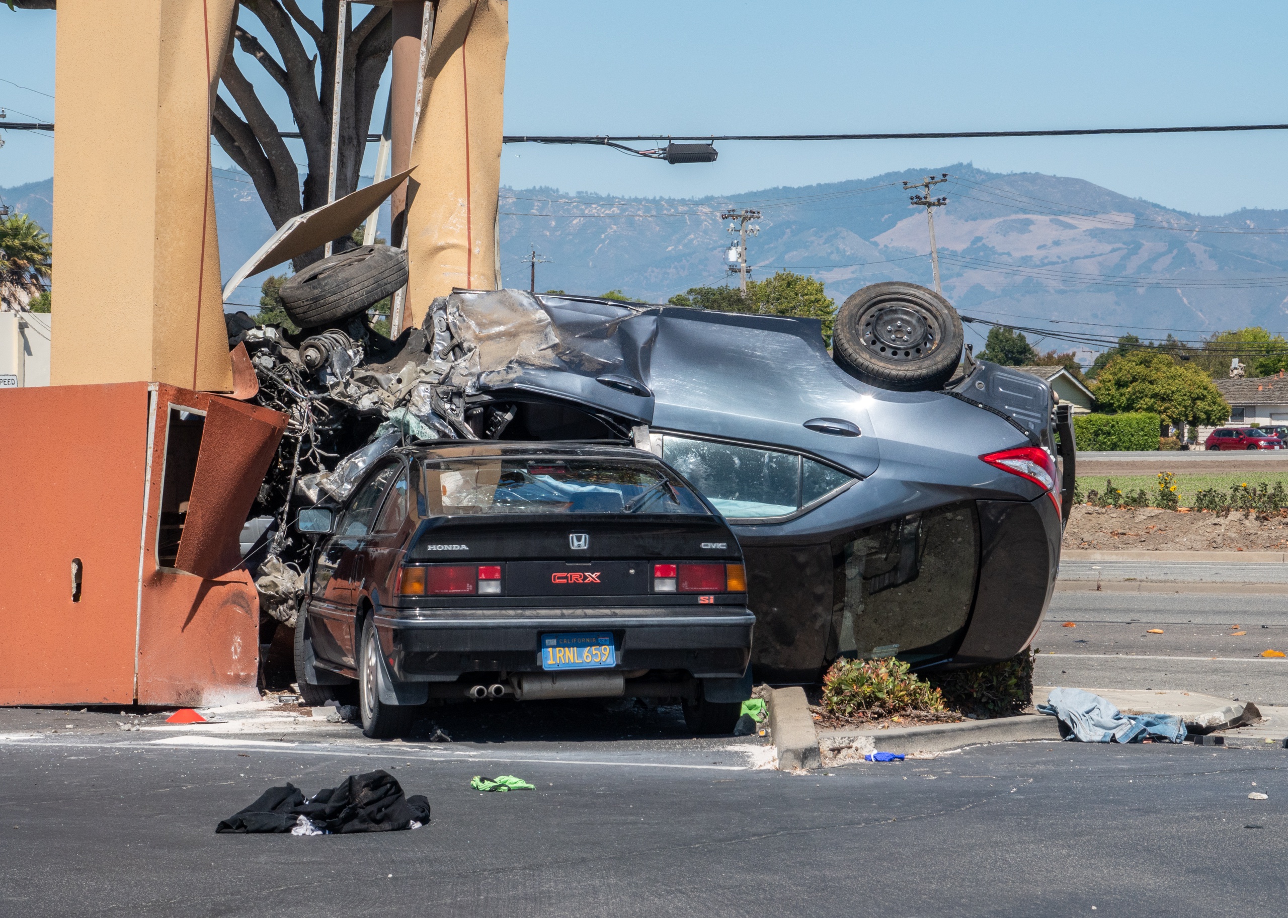 A wrecked car upside down on top of a parked car.