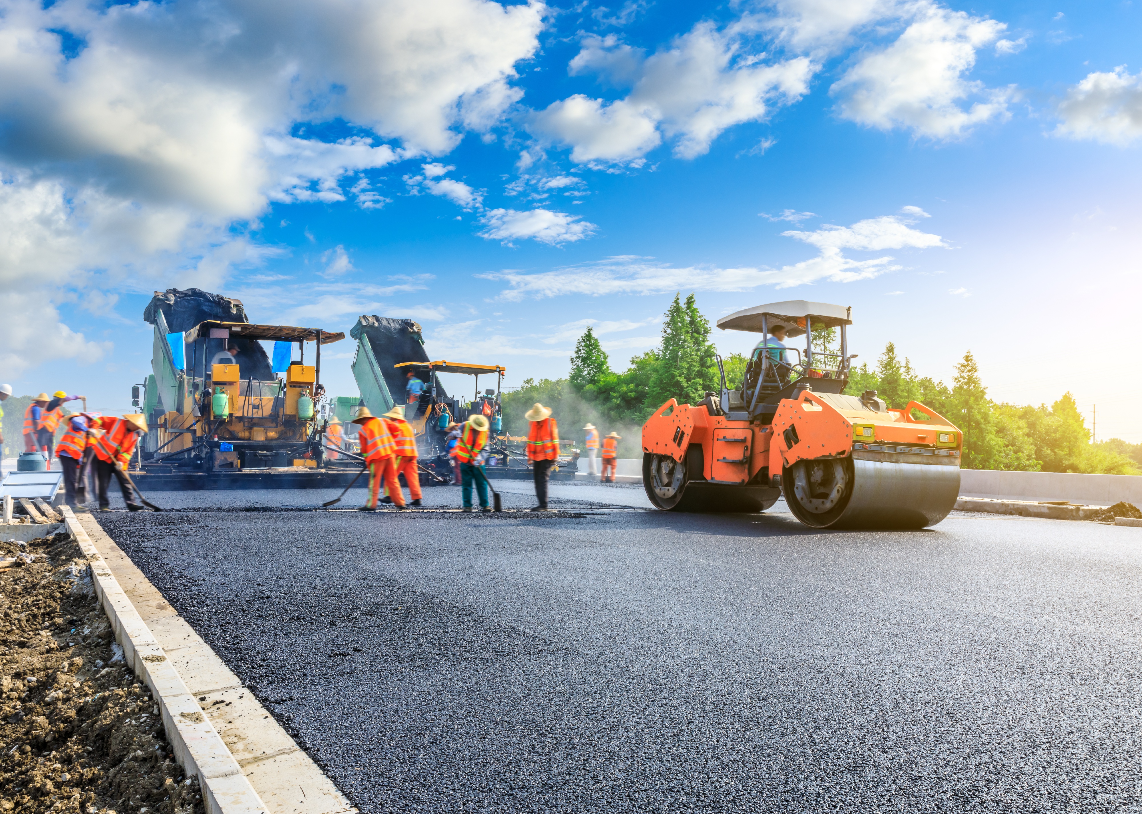 A group of workers laying new asphalt road pavement.