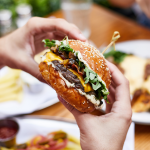 Close up hands holding burger at outdoor restaurant table.
