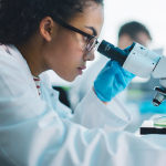 Woman working behind microscope in lab.