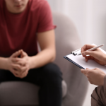 Therapist writing on a clipboard in a session with a patient.