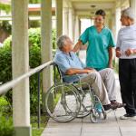 Two seniors talking to a nurse in the garden of a nursing facility.