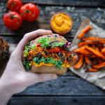 A plant-based sandwich is held in front of a backdrop of other plant foods.