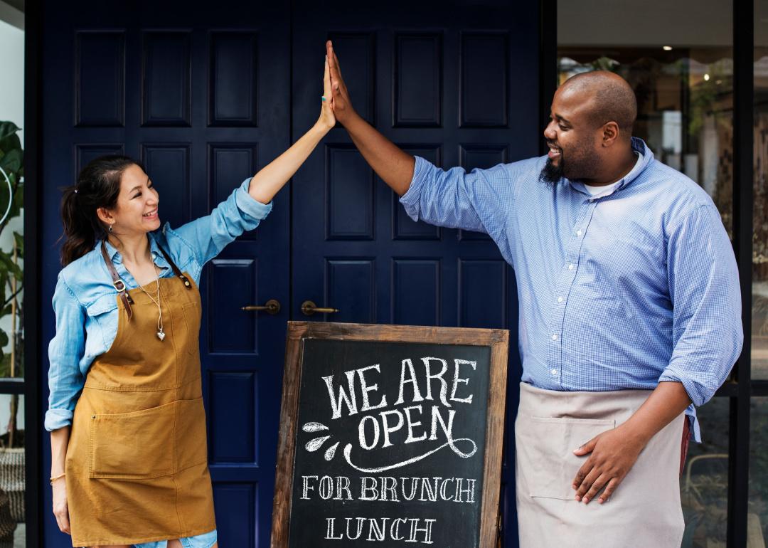 Cheerful business owners standing with 'Open' blackboard.