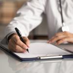 Doctor filling out paper medical records.