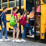 Children boarding yellow school bus with backpacks.