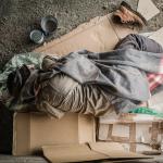 Man wearing sweater and blanket, sleeping on cardboard