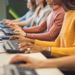 Closeup of a row of diverse workers on computers. The focus is on their hands.