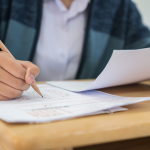 Closeup of student taking an exam at a desk, filling in an answer sheet with a pencil.