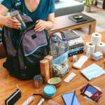 Woman putting cans of food in backpack to prepare for emergency.