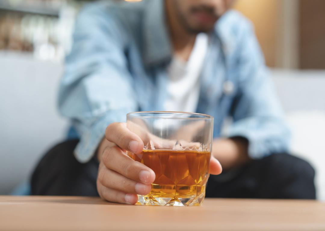 Young man reaching for glass of brown liquor.