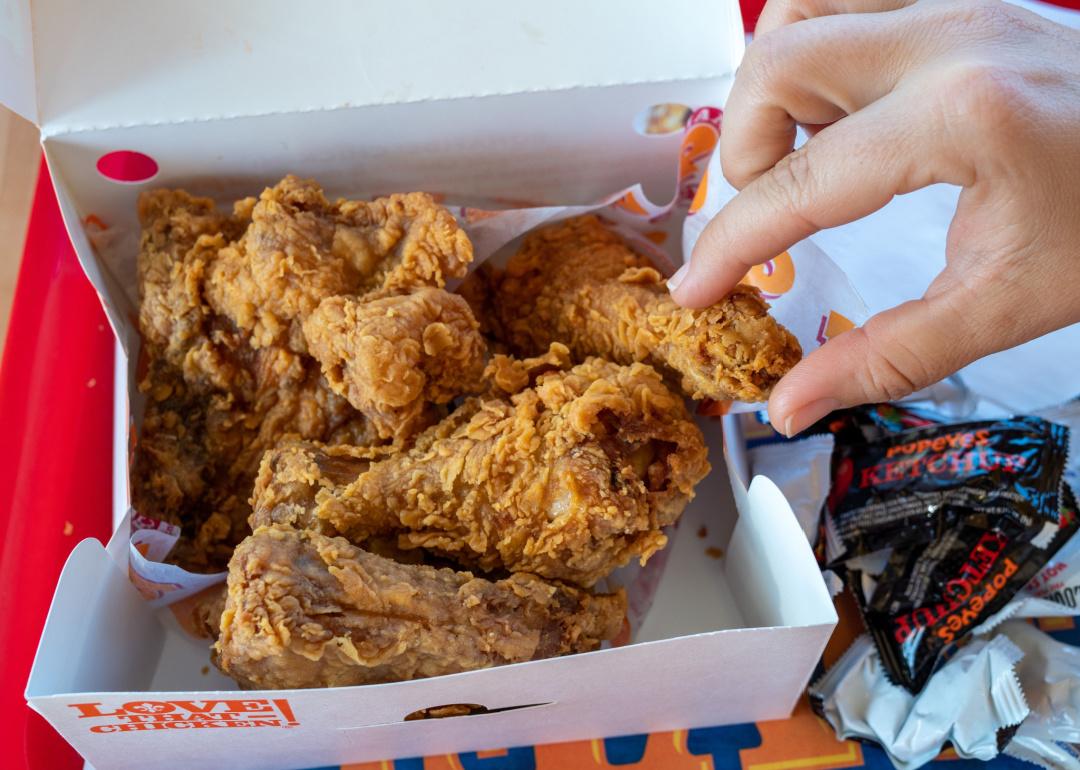 Woman's hand grabbing piece of Popeyes Louisiana Chicken from dinner box in restaurant
