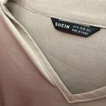 A Shein clothing brand tag in a tan v-neck shirt.
