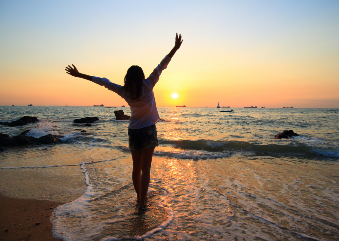 A person stretching at the water's edge at sunset.