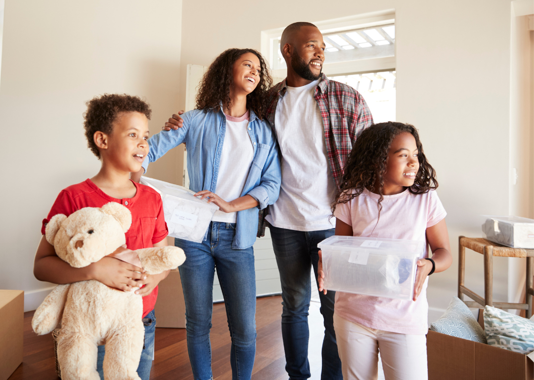 A family of four stands with moving boxes in living room of home.