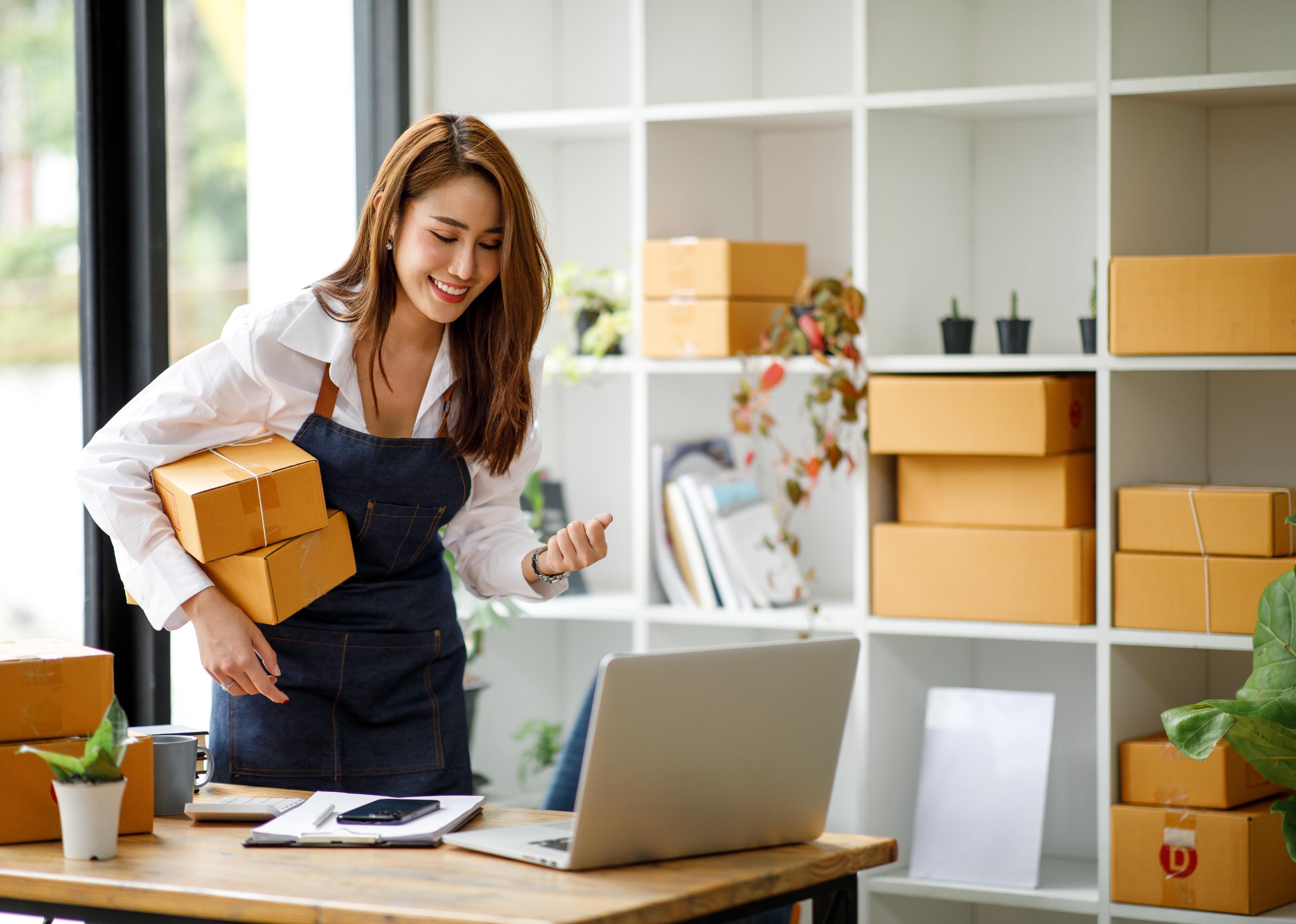 Woman wearing an apron standing in workspace holding boxes.