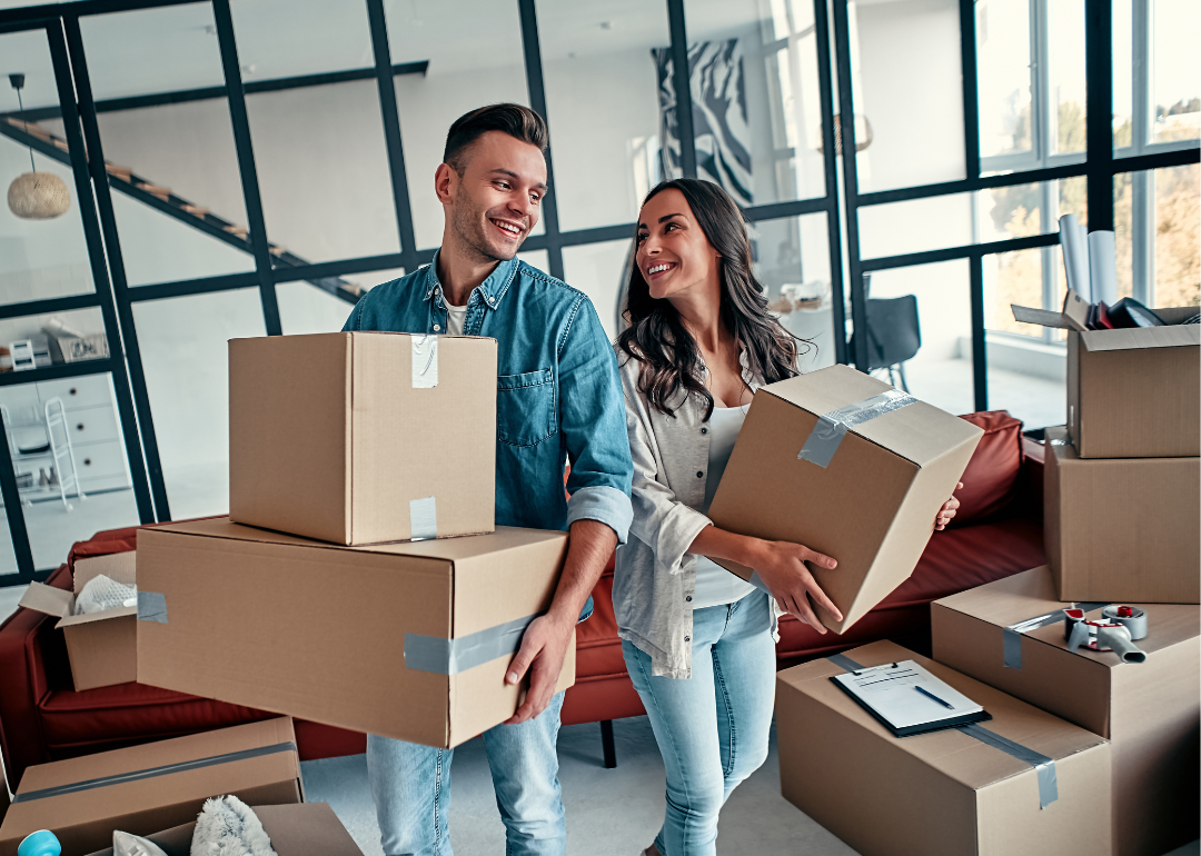 A couple carrying boxes moves into a new home.