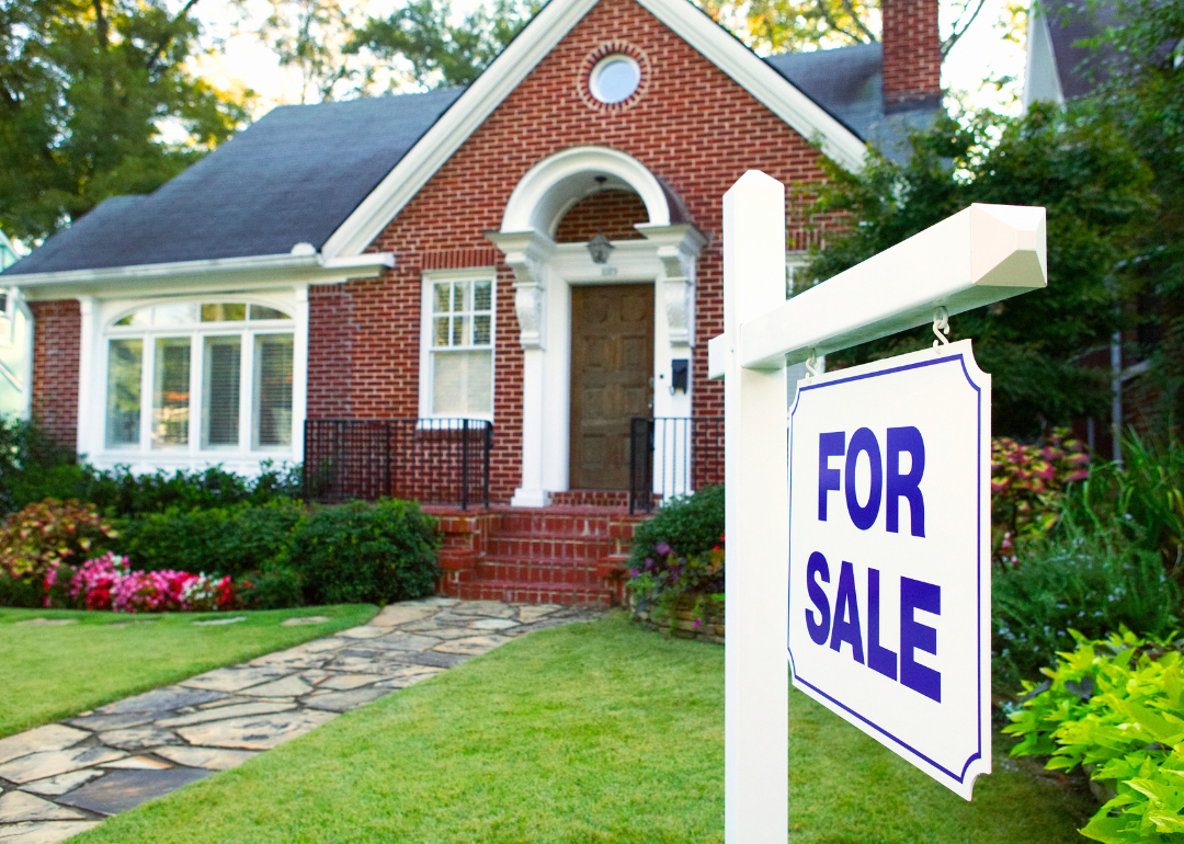A red brick home with a "For Sale" sign in the front yard.