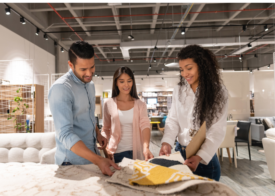 A salesperson shows a couple rug samples in a store.