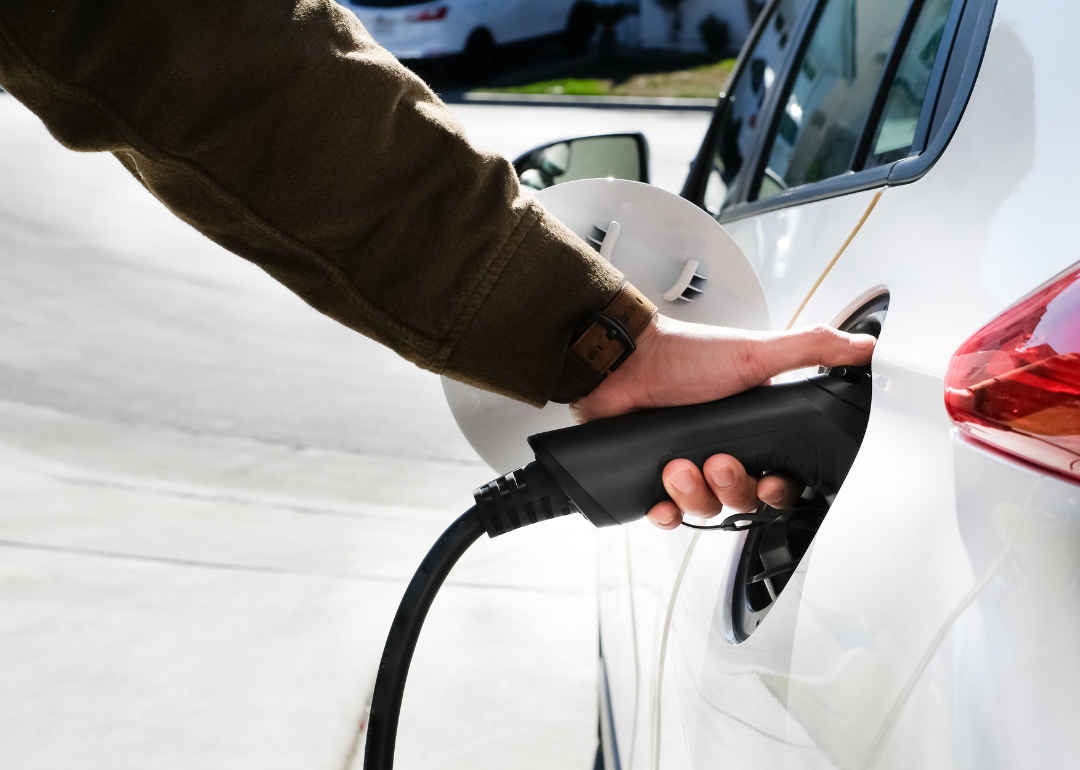 A person plugs in a charger into a white electric car.