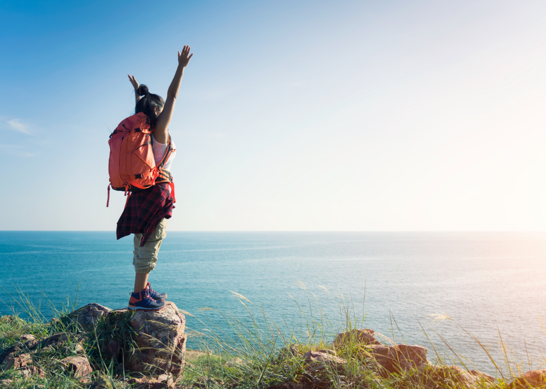 A backpacker standing on the coast with her arm in the air. 