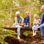 Grandparents and grandchildren sitting on a wooden bridge in the forest, smiling