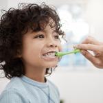 A parent brushing their child's teeth in the bathroom at home.