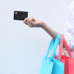 A woman holding a credit card and multi-colored shopping bags against a white background