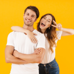 A young couple smiling; the woman holds up a peace sign