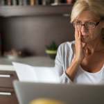 A woman sits at a desk and looks worriedly at a bill she's received