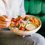 A person eats a bowl of assorted vegetables .