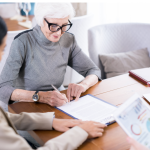 A older woman in a gray sweater fills out a will