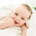 Smiling baby with blue eyes wrapped in a white blanket.