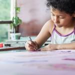 Closeup of a little girl coloring with a purple pencil.