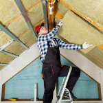 A man stands on a ladder and installs insulation in his attic