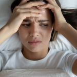A person in bed holding their head after being awoken by a hypnic jerk.