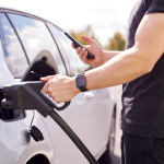 A man charges an electric vehicle while looking at his smartphone