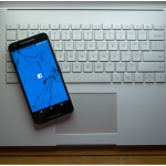 A cracked phone with the Facebook app loading sitting on a laptop.