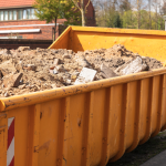 Debris from destruction of a building in a yellow container on a work site.