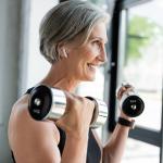 Smiling person with gray hair lifts weights while wearing wireless headphones.