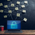 A laptop sitting on a desk beside a red cup of coffee; above the laptop are several post-its with locks drawn on them, connected by chalk lines to symbolize online security