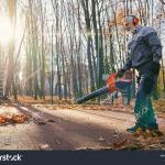 man using leafblower in forest while sun sets behind